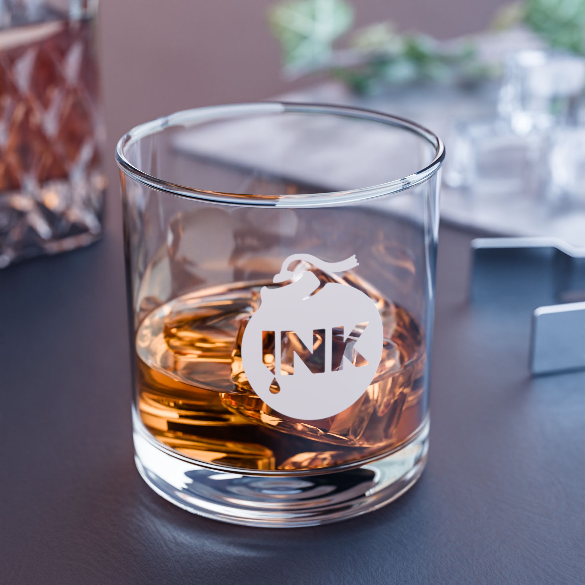 Product photography of the InkBomb Engraved Rocks Glass sitting on a table with bourbon and ice inside it